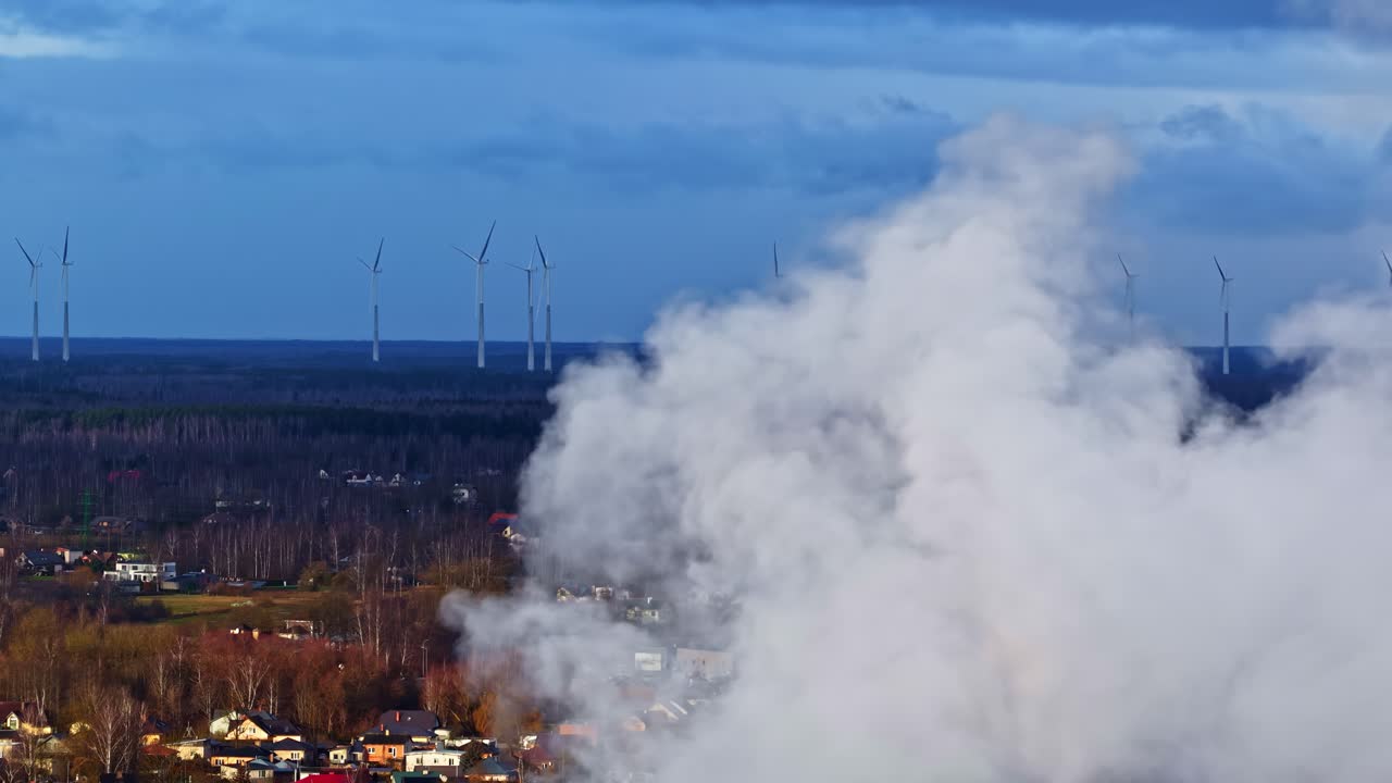 Vista aerea di una colonna di vapore bianco che si alza sopra un paesaggio con turbine eoliche