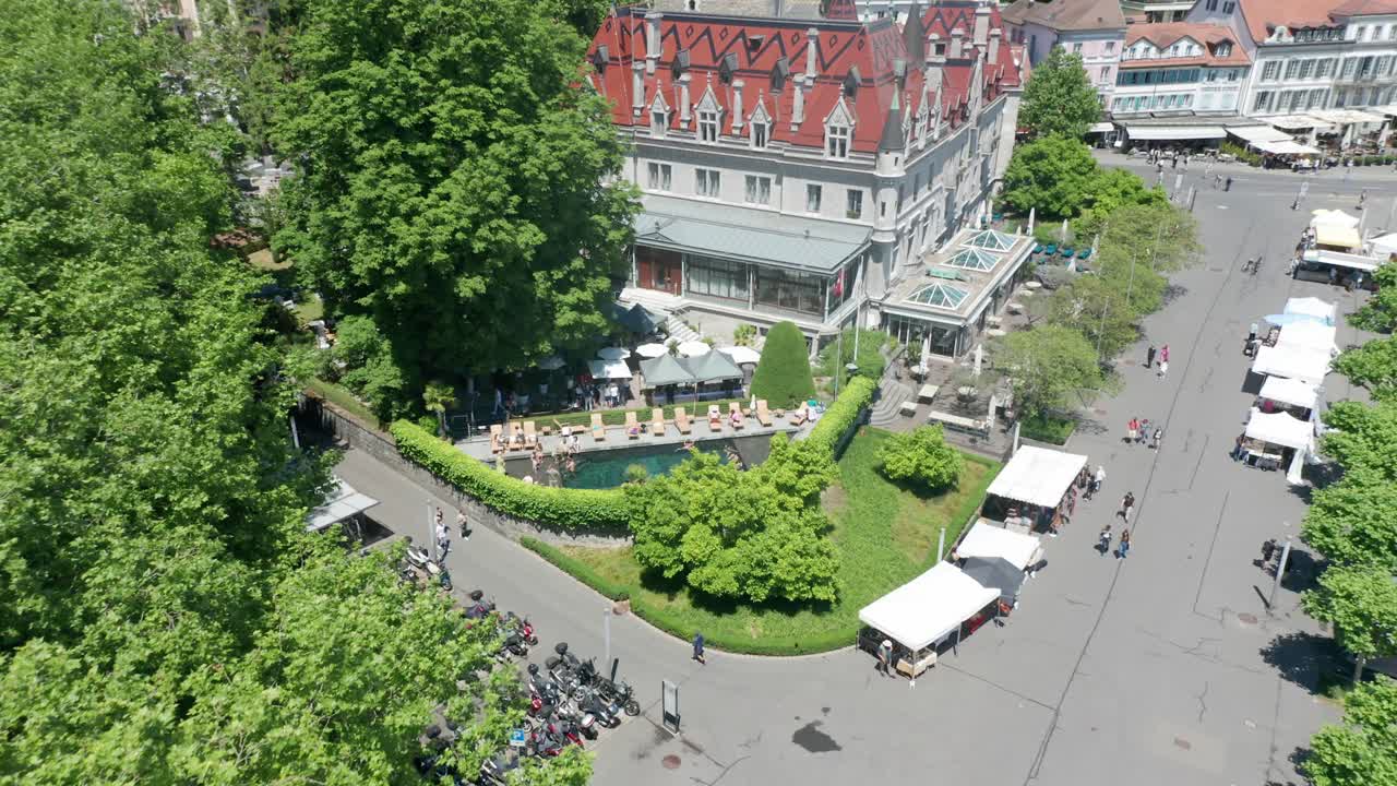 Drone slowly flying backwards from outdoor swimming pool and revealing Chateau d'Ouchy in Lausanne, Switzerland