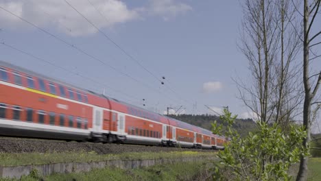 orange deutsche bahn train speeding through a rural landscape with wind turbines in the background, daylight