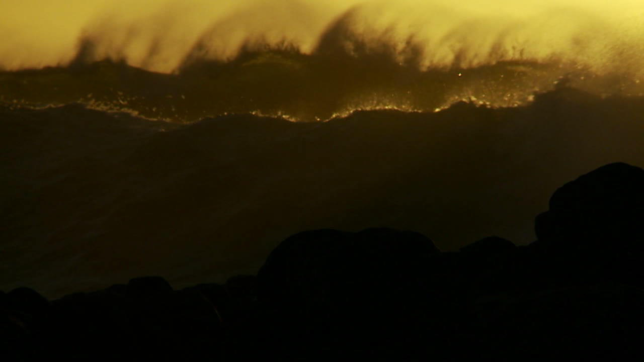 큰 주황색과 검은색 파도가 해질녘 슬로우 모션으로 볏과 부서짐