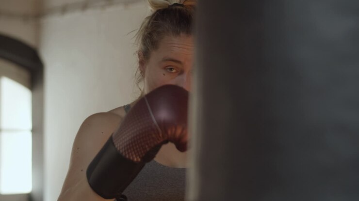 Vista frontale di una donna concentrata che colpisce il sacco da boxe in palestra.