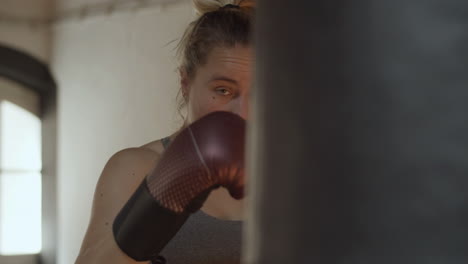 front view of focused woman hitting heavy bag in gym