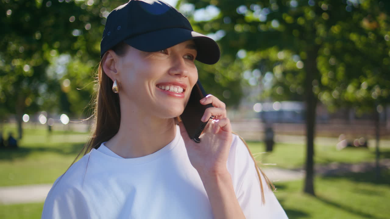 Sporty girl talking cellphone in green park closeup. Cheerful woman calling