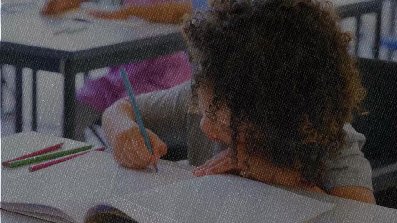 Camera cropping right, curly boy picking colored pencils and drawing to complete worksheet