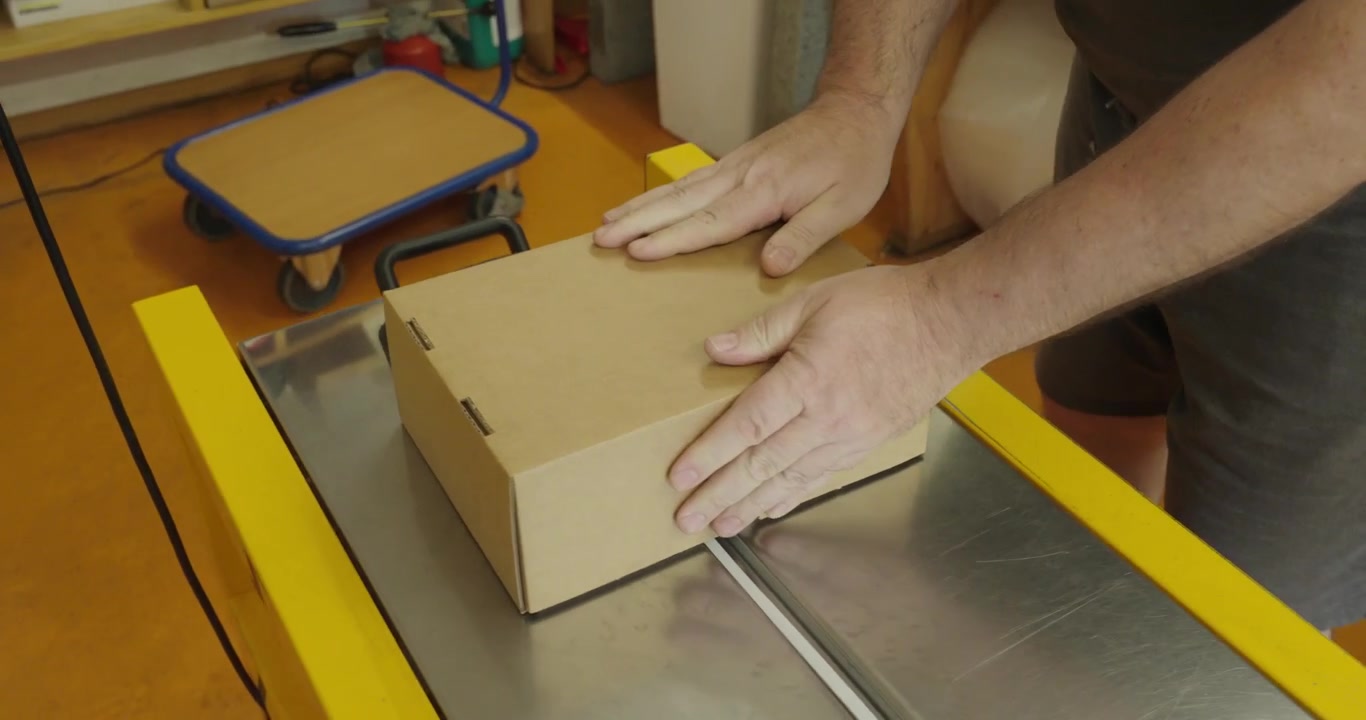 Person closing a cardboard box filled with packaging material, preparing a parcel for shipping and delivery.