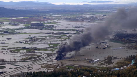 vehículos en llamas con humo negro llenando el cielo en medio de las inundaciones masivas en abbotsford, bc, canadá