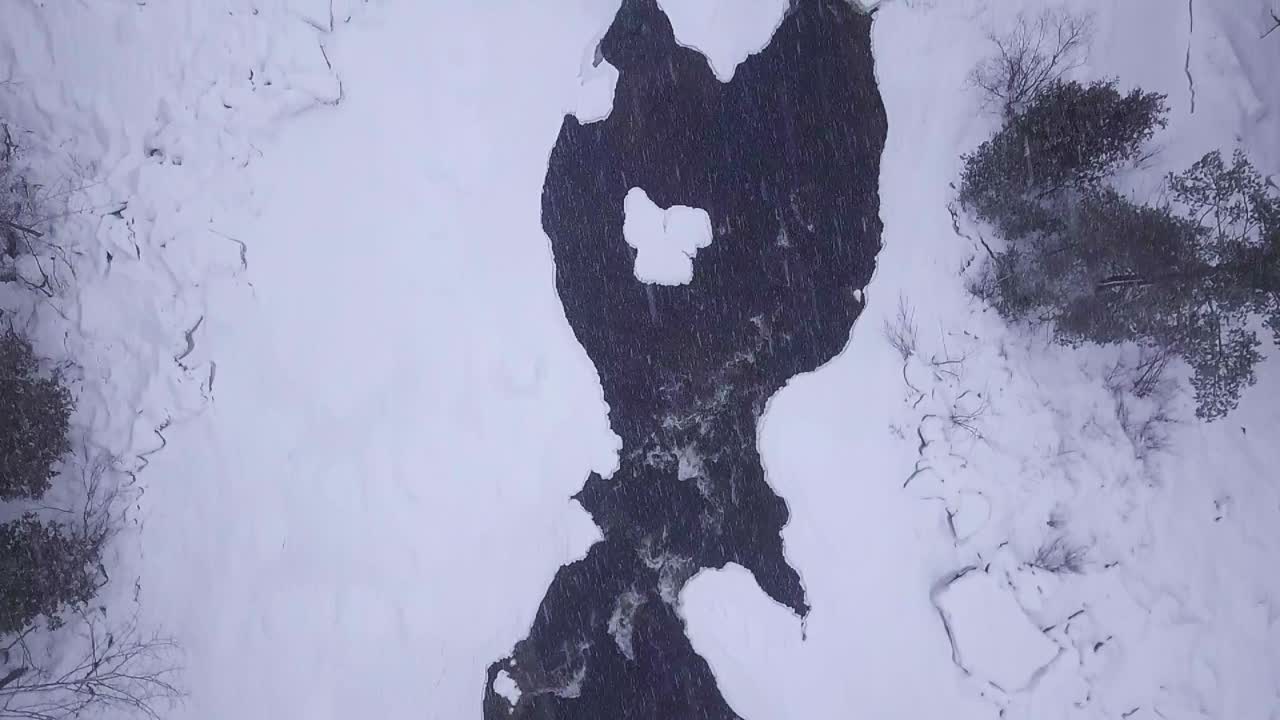 SLOW MOTION TOP DOWN af en isfyldt flod med to små sneklædte øer under en snestorm filmet med drone