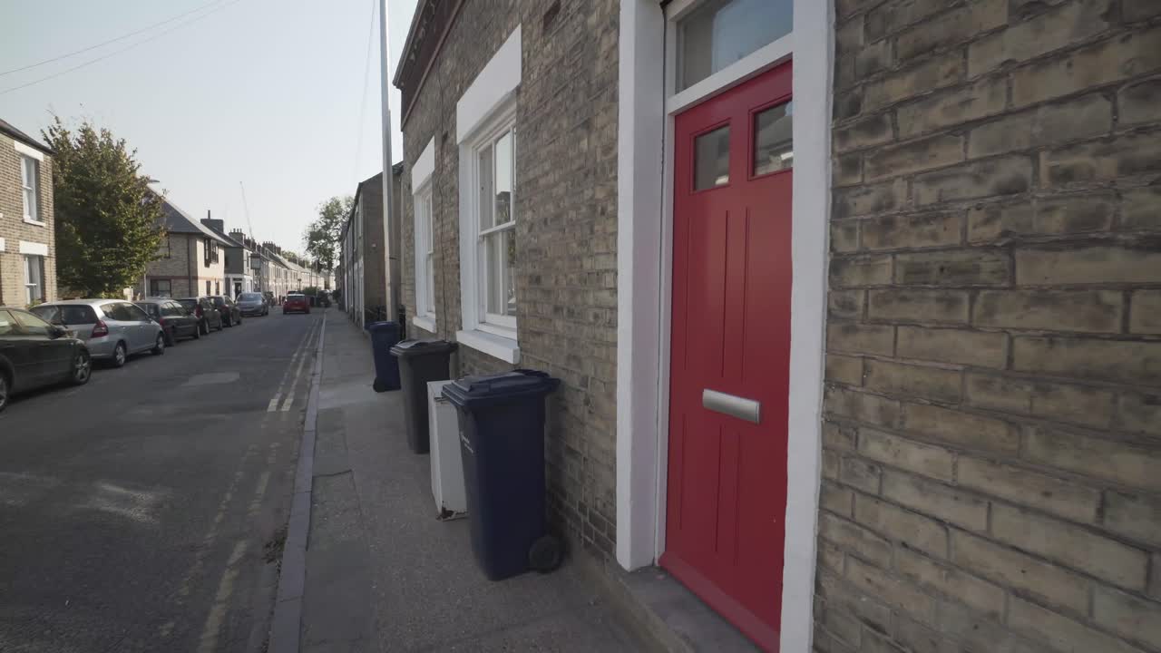 Steady wide angle shot of typical street in cambridge city england uk. Beautiful house entrance with red door and white frame. Recycle bins on the sidewalk