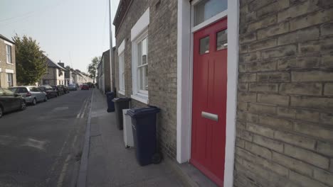 steady wide angle shot of typical street in cambridge city england uk. beautiful house entrance with red door and white frame. recycle bins on the sidewalk