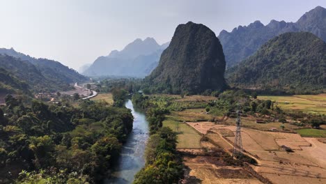 pull out drone shot reveals dramatic karst cliffs rising above nam song river and patchwork farmlands near pha tang, north of vang vieng, in central laos during the dry season