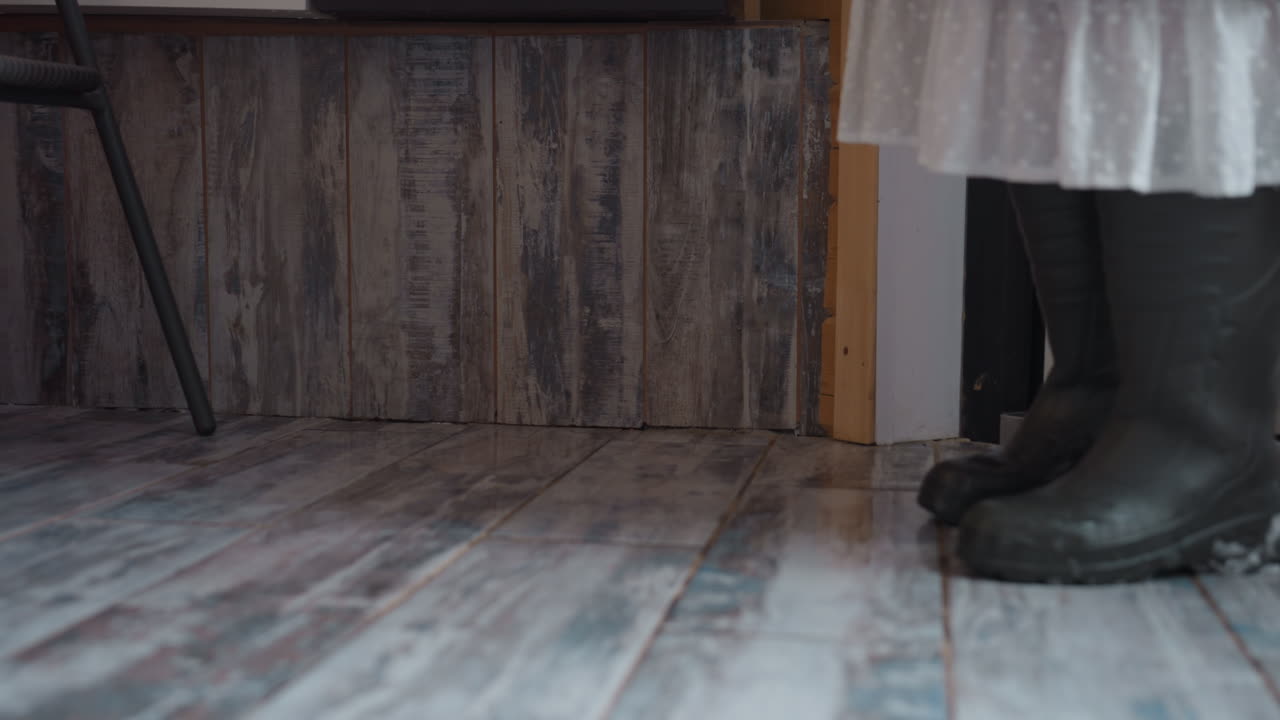 Woman stepping through doorway with bucket heaped with fresh snow, dipping fingertips into powdery mound, rustic tiled floor underfoot, footprints glinting in melting droplets under soft winter light