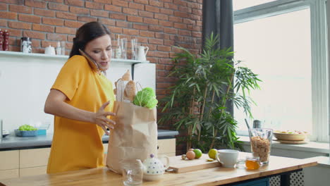 mujer llevando bolsas de compras a la cocina. chica bonita hablando por teléfono en casa.