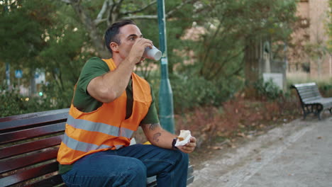 uniform foreman drinking tea enjoying break at wooden bench alone. man resting