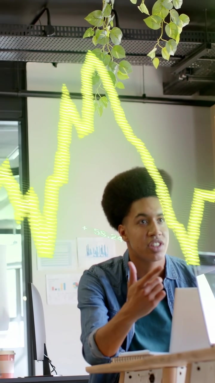 Vertical video: Seated man tracking neon chart spike pointing as peer passes, talking for IT review