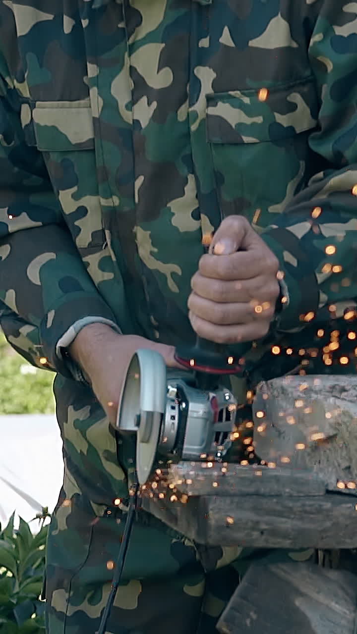 worker in uniform uses disc saw for cutting long metal detail of fence in country house yard