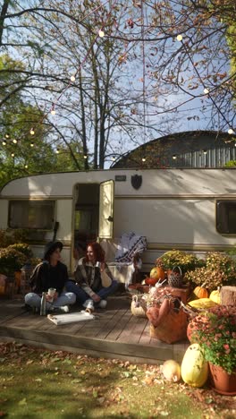 two women enjoying a cozy autumn picnic by a campervan