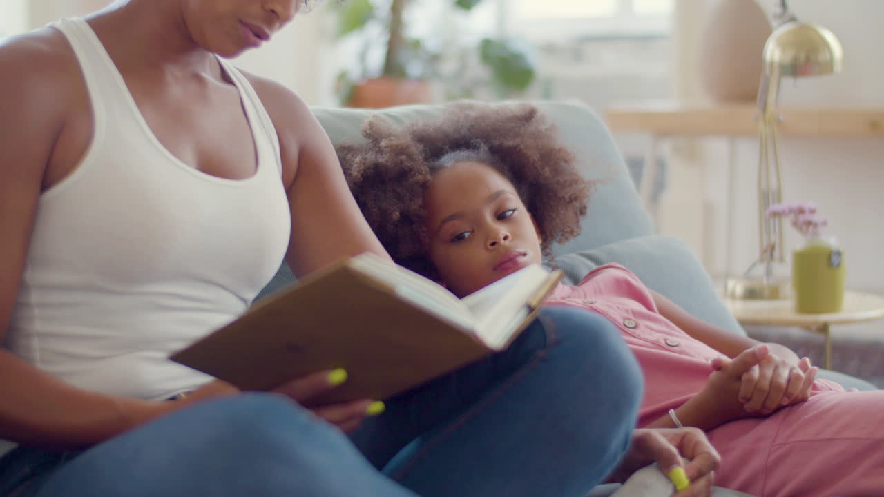 African American woman reading fairy tales to her tired child at home
