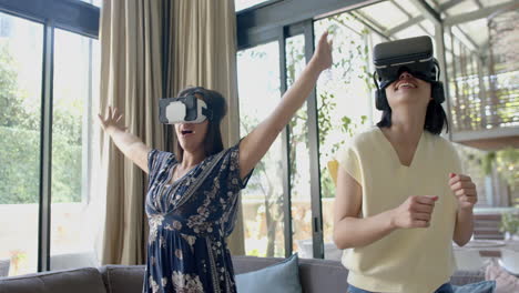 happy asian female friends using vr glasses and dancing in sunny living room, slow motion