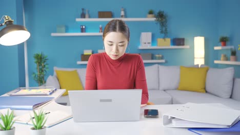 젊은 아시아 여성이 집에서 노트북에 집중하고 있습니다.