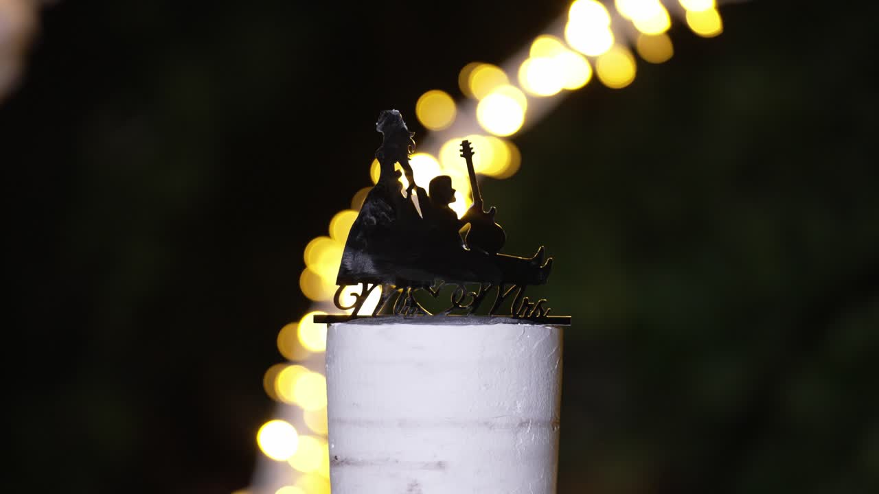 Silhouette cake topper of a couple with a guitar, glowing under soft bokeh lights