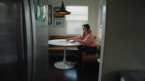 Woman-at-Home-in-Pink-Sweater,-Sitting-at-Kitchen-Table-Sorting-Through-Bills-and-Receipts