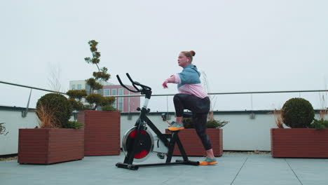 Gesunde-Kaukasische-Frau,-Die-Training-Auf-Einem-Stationären-Fahrrad-Im-Fitnessstudio-Auf-Dem-Dach-Des-Hauses-Durchführt