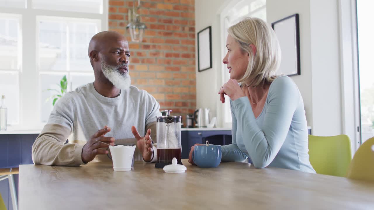Mixed race senior couple talking to each other while having coffee at home