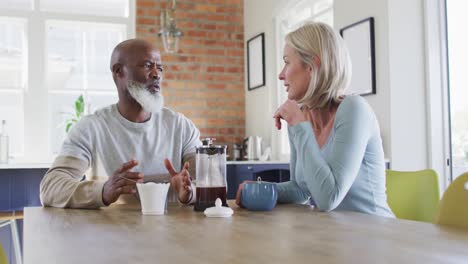 mixed race senior couple talking to each other while having coffee at home