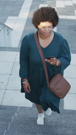 plus size biracial woman walking on stairs with smartphone in city