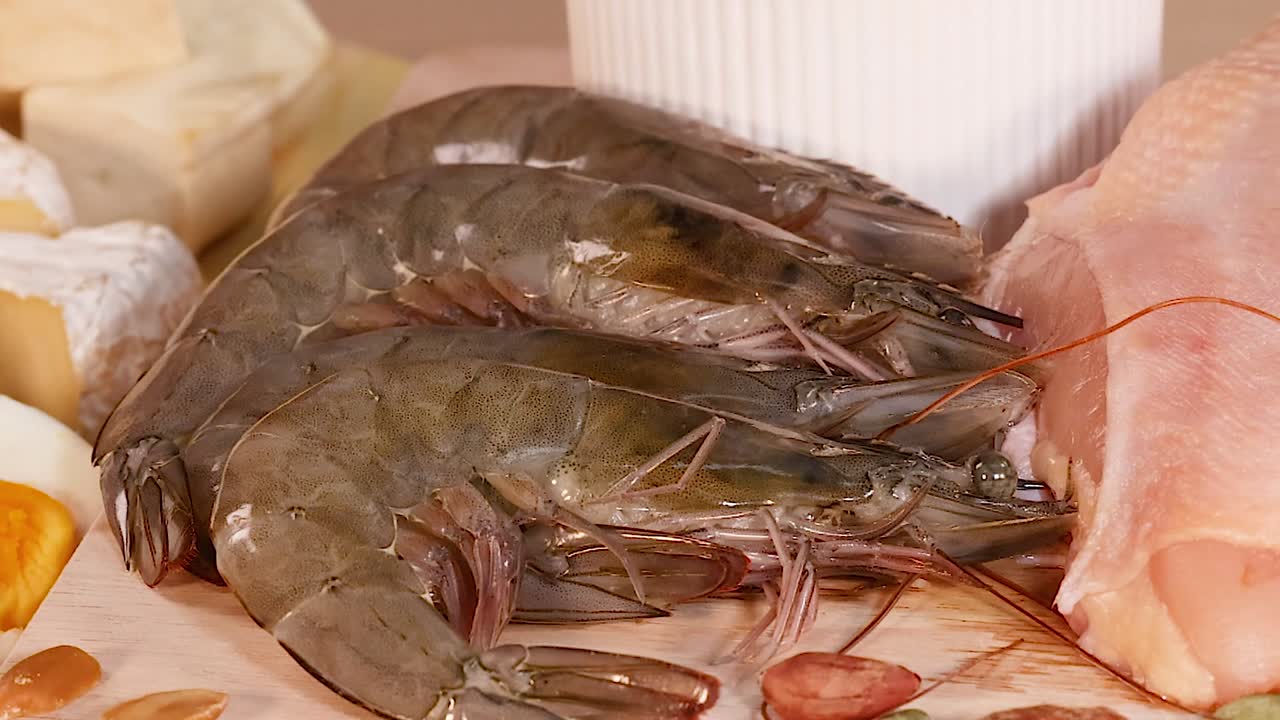 A slow zoom out reveals raw shrimp, chicken breast, eggs, and nuts on a board