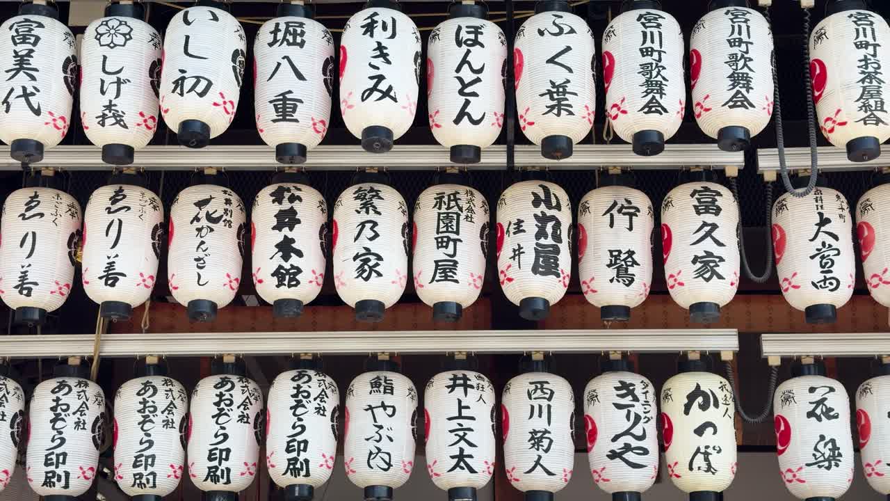 File di lanterne di carta bianche con calligrafia nera pendono in un santuario tradizionale di Kyoto.