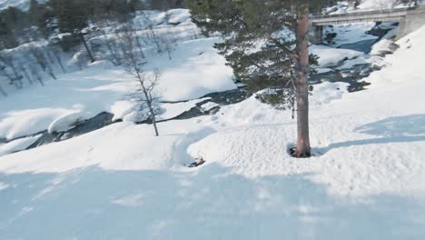 fpv vuela cerca del árbol y debajo del puente de piedra en el paisaje invernal de noruega con un río helado