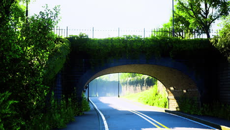quiet morning on a winding road under a stone bridge surrounded by greenery
