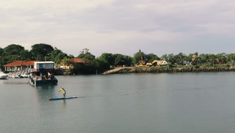 A-paddleboarder-hastily-paddling-past-the-font-of-a-barge-on-his-morning-exercise-routine,-the-vessel-captain-heading-out-to-start-his-morning-shift-and-collect-his-first-load-of-cargo,-Panama-City