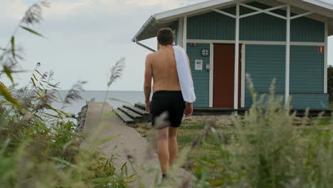 walking man with towel runner athletic going for swim cold sea water beach cabin cool down cloudy day sauna spa relaxing relax runner running athlete training triathlon lonely alone guy sneakers trunk