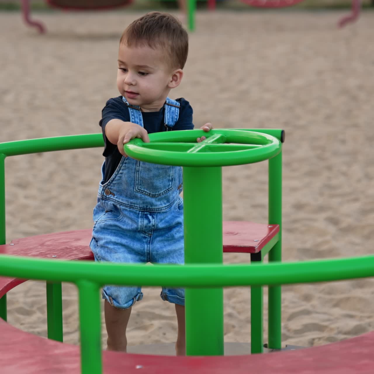 Adorable cute baby sitting on a merry go round. Little Caucasian child spending time on the playground in summer