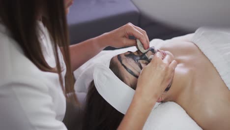 caucasian woman lying back while beautician gives her a face mask