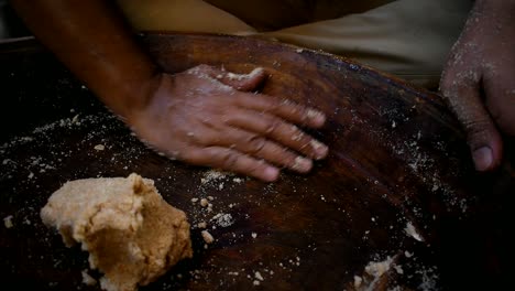 close up of a mans hand kneading flourcdough in a old wooden plate