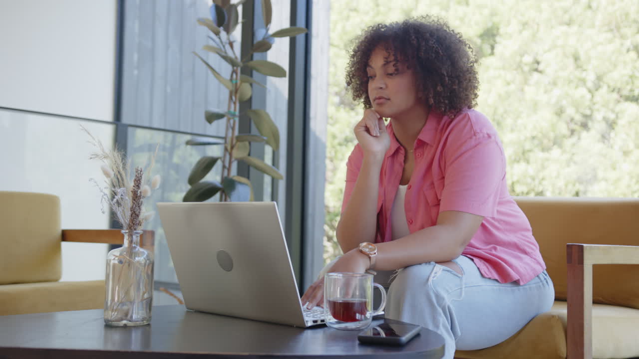 Working from home, woman using laptop and drinking tea, looking thoughtful
