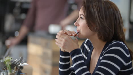 mujer sentada en un café, bebiendo con una pajita, de cerca