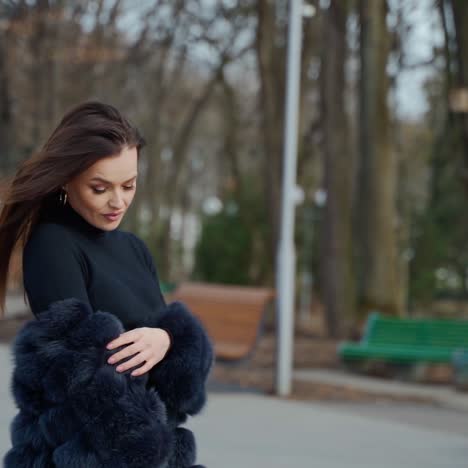 fashionable girl with long hair looking at camera outdoors. portrait of attractive young woman in fur coat poses on camera on the park background.