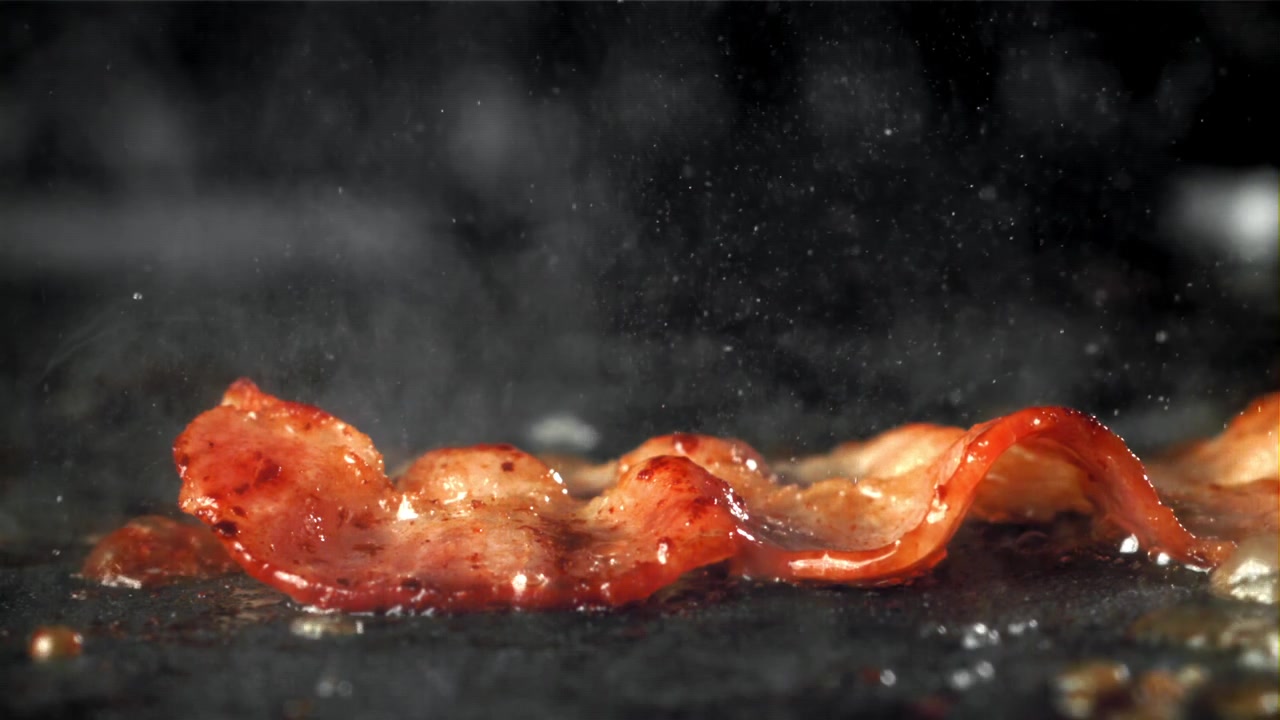 Primo piano di pancetta che frigge e sfrigola su una piastra calda