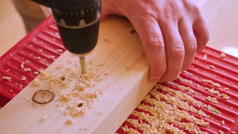 a male hand drills holes in a square timber with a cordless screwdriver