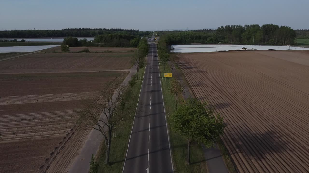 Aerial footage of a rural road with a few cars passing by in Europe on a sunny day with the setting sun