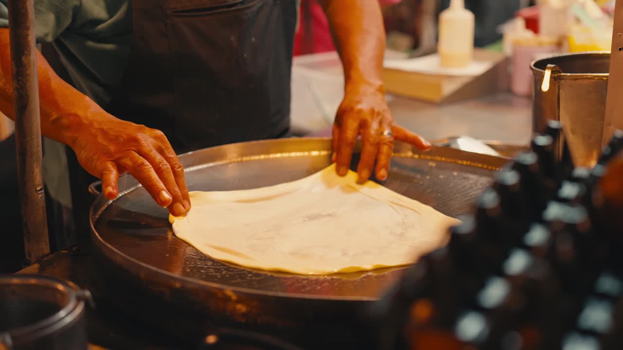 Street food vendor cooking roti dough on a hot metal pan at night time