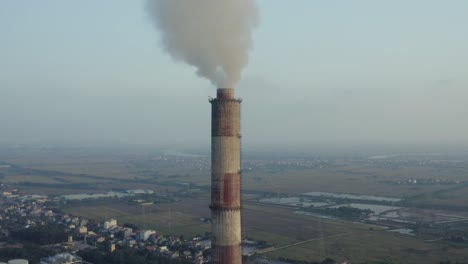 Drone-view-of-the-chimney-are-blowing-smoke-into-the-sky,-on-the-sunset