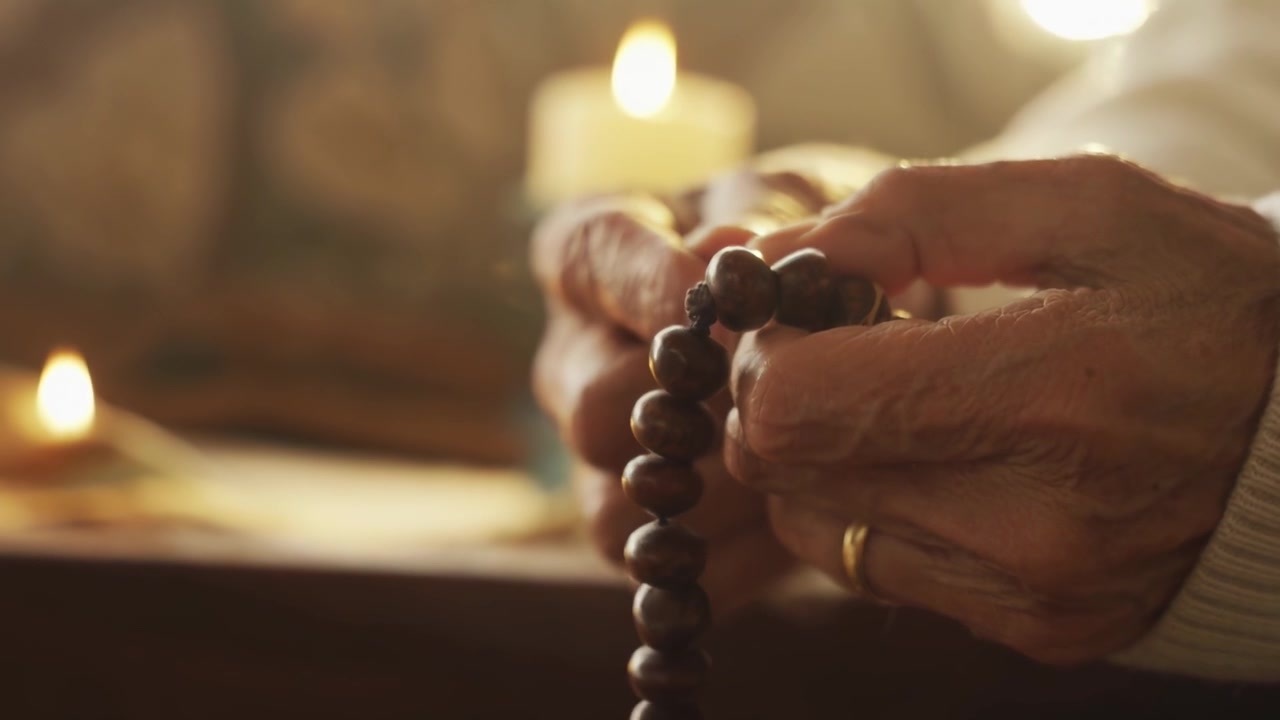 Elderly Person Praying with Wooden Prayer Beads by Candlelight