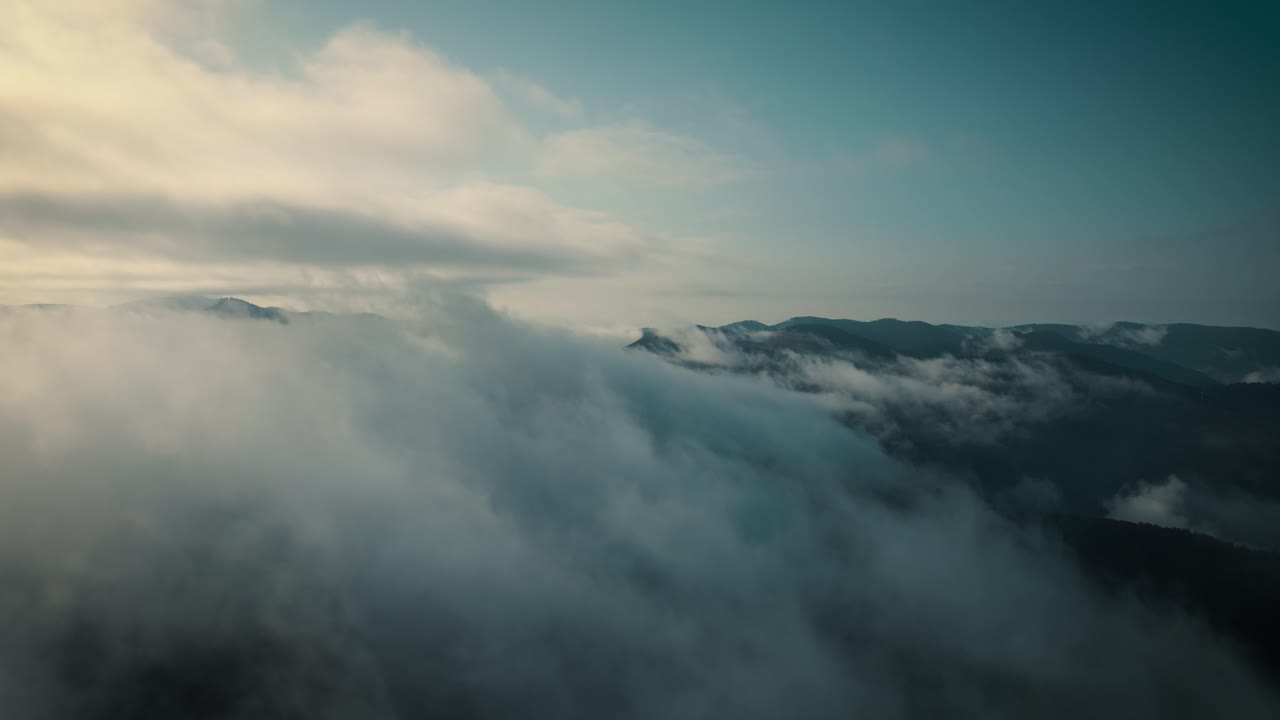 Aerial flying forwards among clouds, mountains in background
