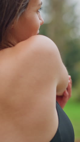 Close-up view of woman in black neck top stretching arms outdoors, blurred background showing greenery and trees, focused on wellness and fitness routine