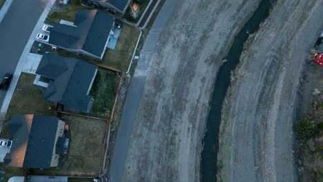 Luftaufnahme-Von-Oben-Nach-Unten-Eines-Bewässerungsgrabens,-Der-Hinter-Wohnhäusern-Verläuft